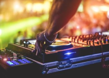 Dj mixing outdoor at beach party festival with crowd of people in background - Summer nightlife view of disco club outside - Soft focus on hand fingers - Fun ,youth,entertainment and fest concept