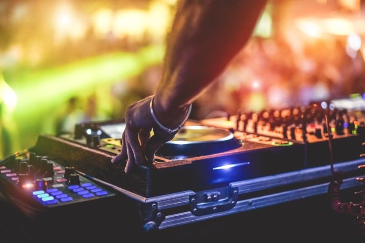 Dj mixing outdoor at beach party festival with crowd of people in background - Summer nightlife view of disco club outside - Soft focus on hand fingers - Fun ,youth,entertainment and fest concept