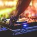 Dj mixing outdoor at beach party festival with crowd of people in background - Summer nightlife view of disco club outside - Soft focus on hand fingers - Fun ,youth,entertainment and fest concept